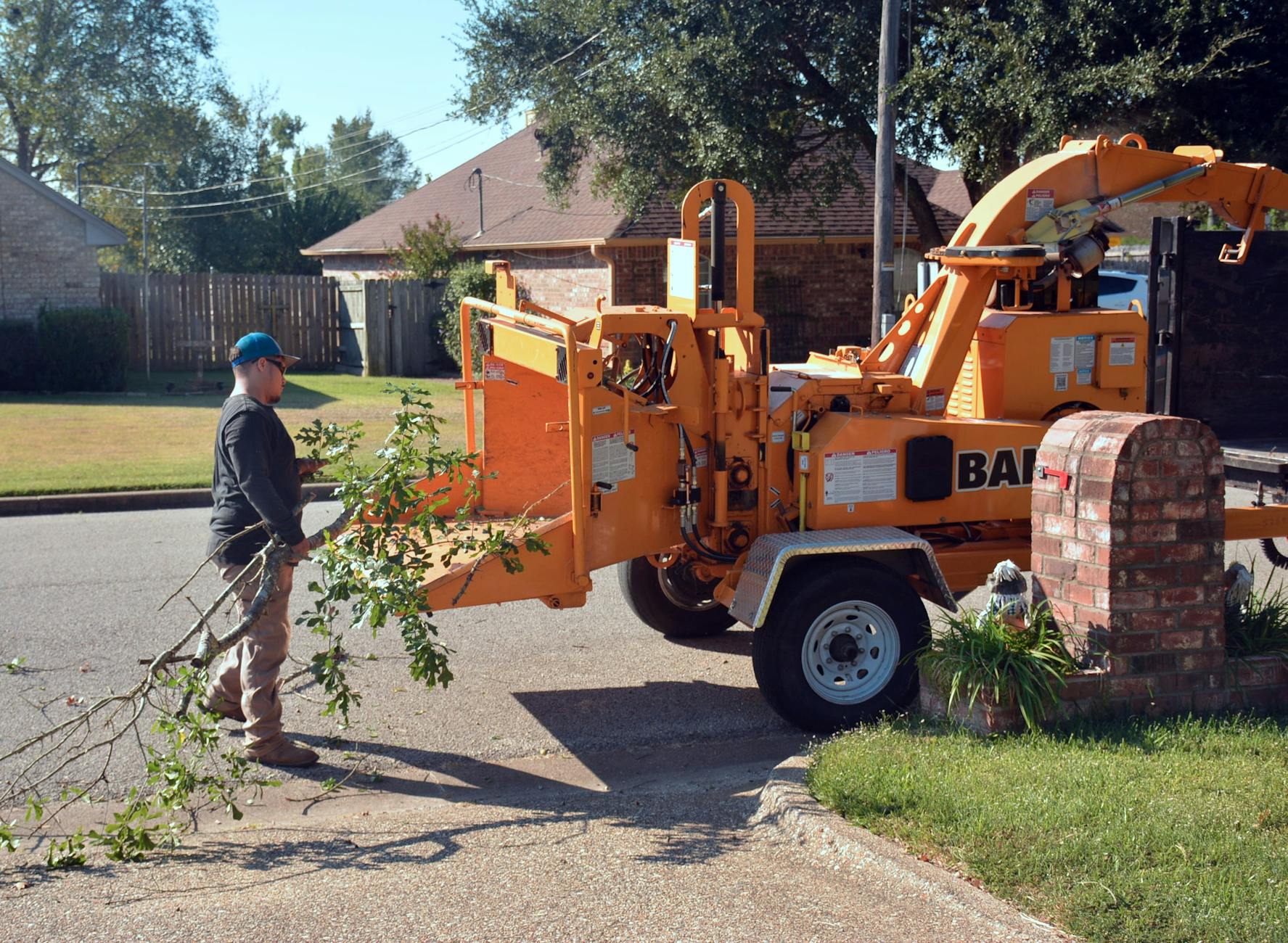 A professional tree removal crew carefully lowering a large oak limb using ropes and rigging on a steep residential lot.